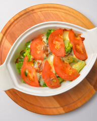 Baked mixed vegetable casserole with broccoli and tomatoes. Served in a white pot over white background.