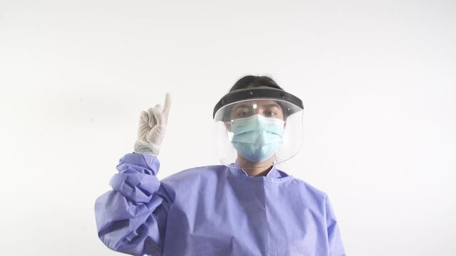 Female surgeon in full protection clothes with medical mask Shows A Forefinger Up in gloves. Covid-19 pandemic in hospital.