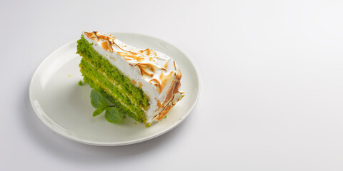 A piece of green tea cake. One piece of matcha tea cake with cream frosting and mint leaf served on around white plate.