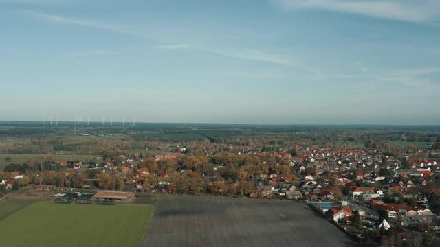 Small town in the north of Germany, approach over the field with a view to the straight horizon of the plain with a few windmills, aerial view