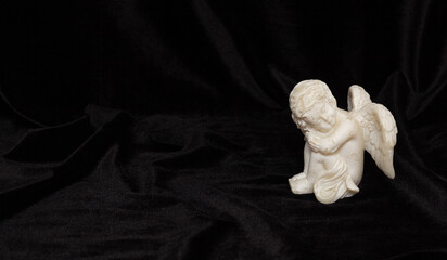 Small angel with wings on a black background, free space for text. Concept of memory of a person,...