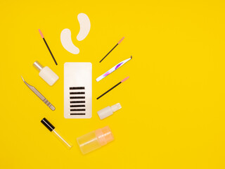 Tools for eyelash extension on a yellow background, top view. Eyelashes, patches, glue, combs. The work of a lashmaker. Self-care, beauty salon. Free space for text.