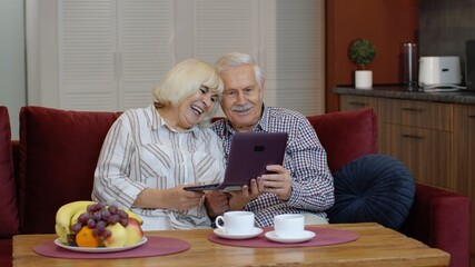 Senior old grandparents couple talking and using digital laptop computer at home. Online shopping. Elderly grandfather and grandmother enjoying time during coronavirus covid-19 lockdown