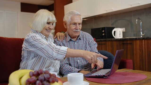 Senior old grandparents couple talking and using digital laptop computer at home. Online shopping. Elderly grandfather and grandmother enjoying time during coronavirus covid-19 lockdown
