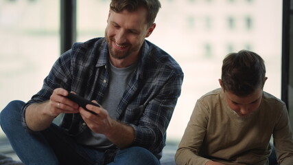 Father and son using smartphones home. Dad and child playing mobile game indoors