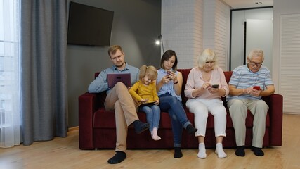 Family sits on the couch with personal gadgets. Spending time at home with mobile phone, tablet, laptop. Addicted to modern technology devices. Social networks, internet obsession concept