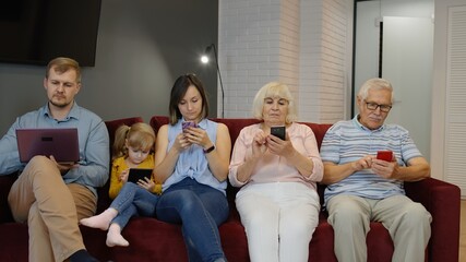 Addicted to gadgets family using mobile phone, tablet, laptop ignoring each other at home. Senior...