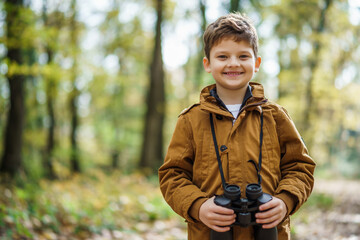 Portrait of boy who is hiking in nature with binoculars in autumn.