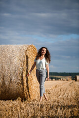 Naklejka na ściany i meble Beautiful girl near hay bales in the countryside. Girl on the background of haystacks