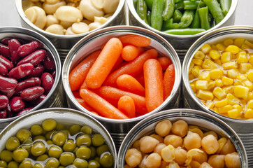 Canned vegetables in opened tin cans on kitchen table. Non-perishable long shelf life foods background