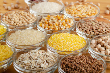 Set of various legumes and grains in glass bowls on wooden kitchen table, non-perishable, long shelf life food concept