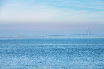 Obraz premium Amid the fog or mist, the Oresund Bridge or Oresundsbron lies on a calm Baltic sea as commuters cross the Oresund strait between the Danish capital Copenhagen and Malmo, Sweden - Dragor, Denmark