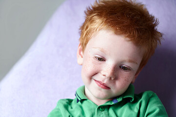 Closeup portrait of a cute red haired freckled little boy in green t-shirt waiting for doctor in...