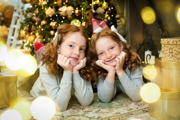 Fototapeta na wymiar two red-haired sisters near the New Year tree. Christmas holiday atmosphere, lights, gifts, smiles