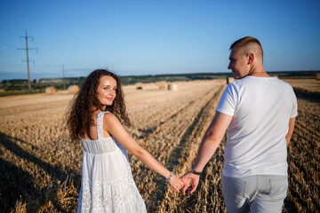 Attractive woman posing in the mown wheat fields with a sheaf in the village. Hay bales on the field after harvest, a place for a photo session of a beautiful Slavic couple