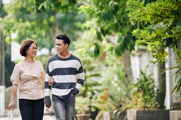 Smiling mother and her teenage son walking in park and discussing news