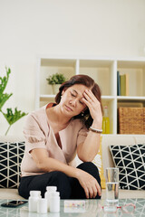 Mature Vietnamese woman suffering from headache looking at containers with pills and supplements in...