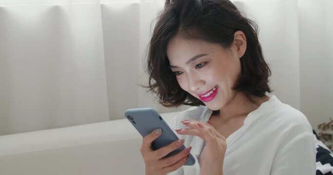 A beautiful young Chinese woman in white blouse using cell phone to send messages to converse with friends and families.Asian woman with short hair playing gadget games and looking up happily.