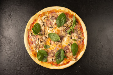 Round hot freshly baked pizza with mushrooms, chicken, basil, onions and cheese lies on a black stone kitchen table