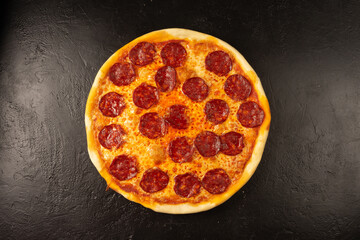 Round hot freshly baked pizza with salami and cheese lies on a black stone kitchen table