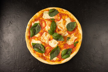 Round hot freshly baked pizza with mozzarella, tomatoes, basil and cheese lies on a black stone kitchen table