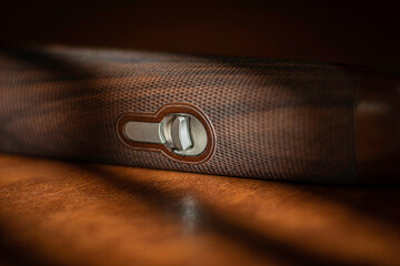 A sporting rifle with a wooden stock lies on a brown background, close-up of the forearm button,...