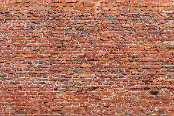 Brick wall made of old crumbling red bricks falling out.