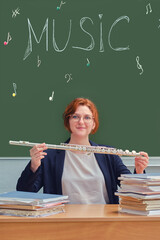 Woman music teacher holds flute in hands in school class and smiles
