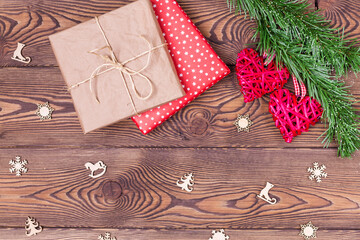 Christmas decor or background for Valentine's Day. Two red hearts from rattan on a spruce branch and a gift wrapped in paper on a wooden table. Top view, copy space.