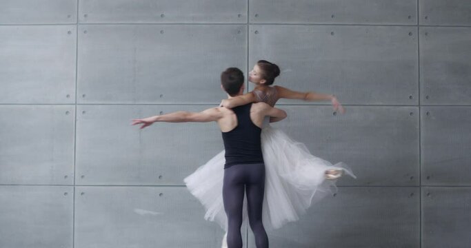 Elegant couple of classical ballet dancers rehearsing a dance on a gray background, romantic dance of ballet dancers, a young couple engaged in choreography.