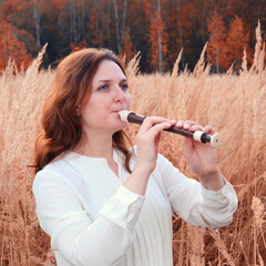A young woman with red hair plays a flute in an autumn grass © Андрей Журавлев