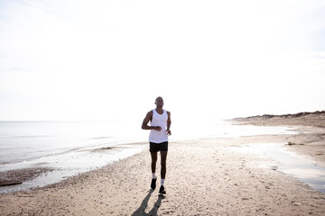 Black young man is jogging on street among the sun shines back light.