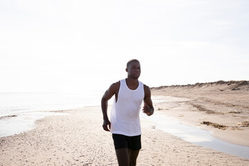 Black young man is jogging on street among the sun shines back light.