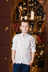 Fototapeta na wymiar nine-year-old boy in a white shirt looks at the camera in a dark room. Handsome