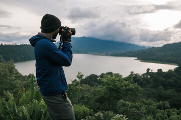 A man traveler, in a knitted hat, photographs the landscape with a camera.