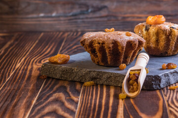 studio lighting. wooden background in retro style, vintage. On it are two muffins and dried apricots sprinkled with raisins. Dried berries are laid in a small spoon.