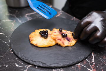 Canned pineapples soaked in caramel with berries on a black plate