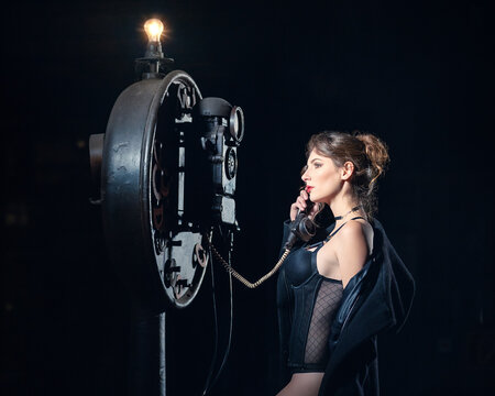 Sexy junge Frau im Dessous, Mantel am alten Telefonapparat bei Nacht im dunklem Raum. 