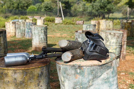 Two marker guns and black protective masks for paintball lying on barrels on open playground