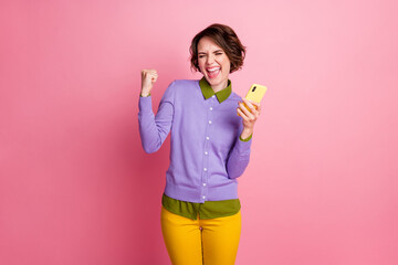 Photo of excited lady hold telephone win free device wear purple jumper yellow pants isolated pink color background