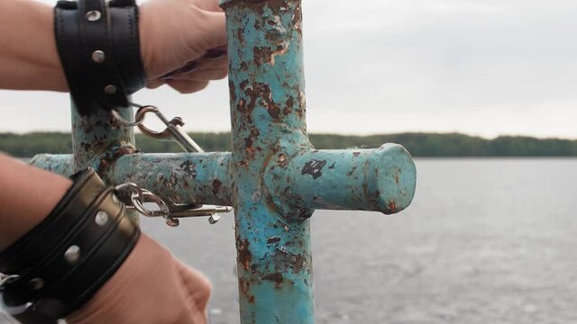 Close up view of woman's hands cuffed to old rusty bollard. Woman can not escape.