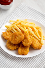 Tasty Fastfood: Chicken Nuggets and French Fries on a plate on a white wooden surface, side view. Close-up.