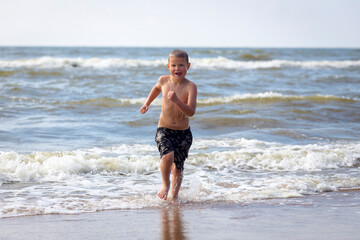 Fototapeta na wymiar Young cheerful boy having fun at sea waves.
