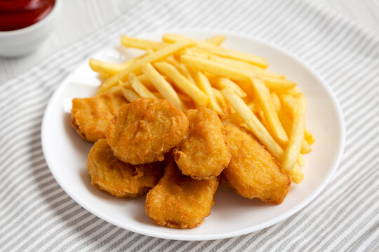 Tasty Fastfood: Chicken Nuggets and French Fries on a plate on a white wooden background, side view. Close-up.
