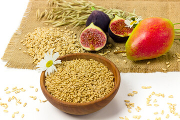 Oat seeds in wooden bowl, oat ears, pear and fresh figs on sackcloth isolated on white background. Organic agriculture concept	
