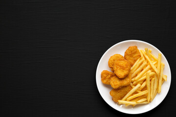 Tasty Fastfood: Chicken Nuggets and French Fries on a plate on a black background, top view. Flat lay, overhead, from above.