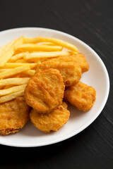 Tasty Fastfood: Chicken Nuggets and French Fries on a plate on a black background, side view. Close-up.