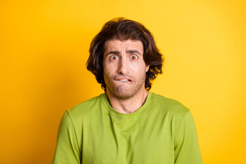 Photo of afraid young man bite lip anxious look camera wear green t-shirt isolated yellow color background