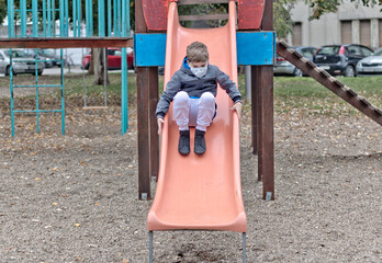 Small boy with protective face mask sliding on the playground.