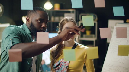 Annoyed mixed race couple working in office. Afro man pointing stickers